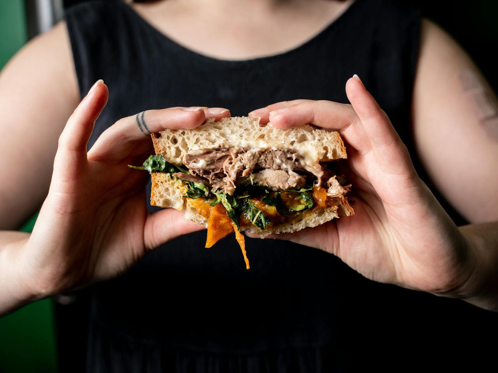 tow hands holding a lamb, relish, spinach, and sourdough  sandwich