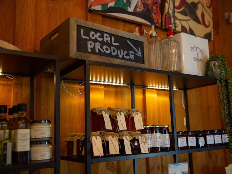 Hand drawn sign that says 'local produce' over rows of jam jars on shelves