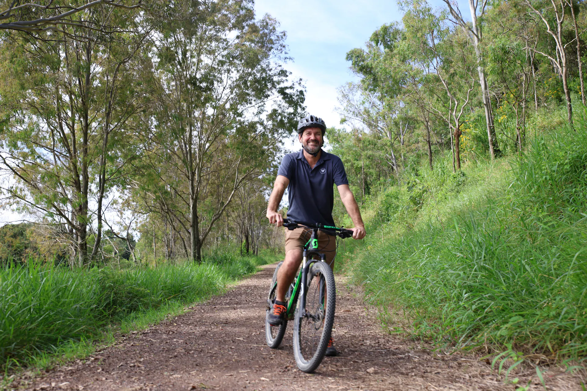 a man is ready to ride his bike on the trail.   Lots of shady trees line the trail.