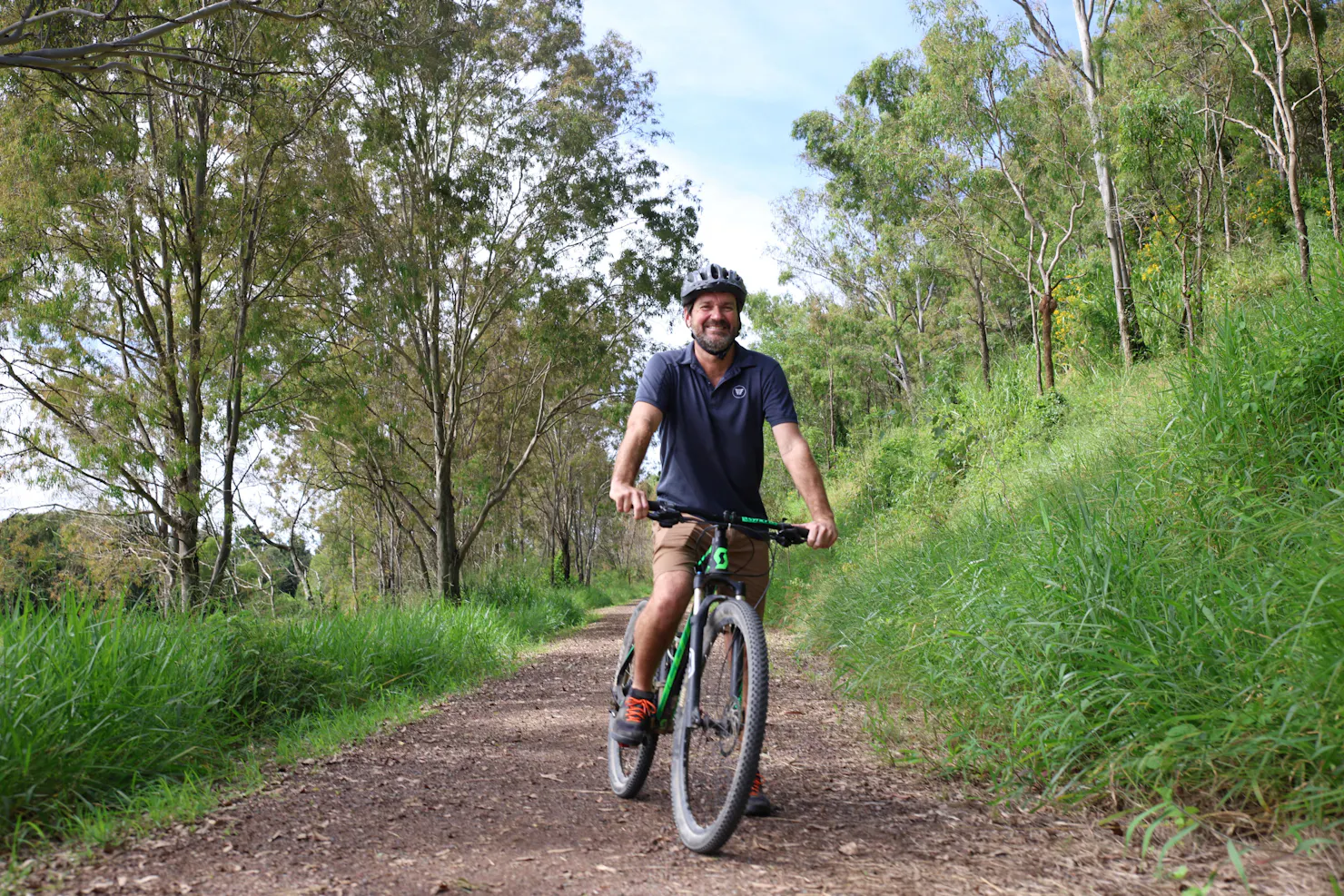 a man is ready to ride his bike on the trail. Lots of shady trees line the trail.