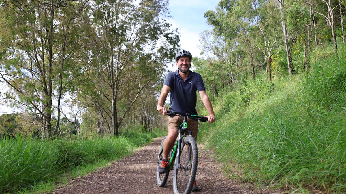 a man is ready to ride his bike on the trail.   Lots of shady trees line the trail.
