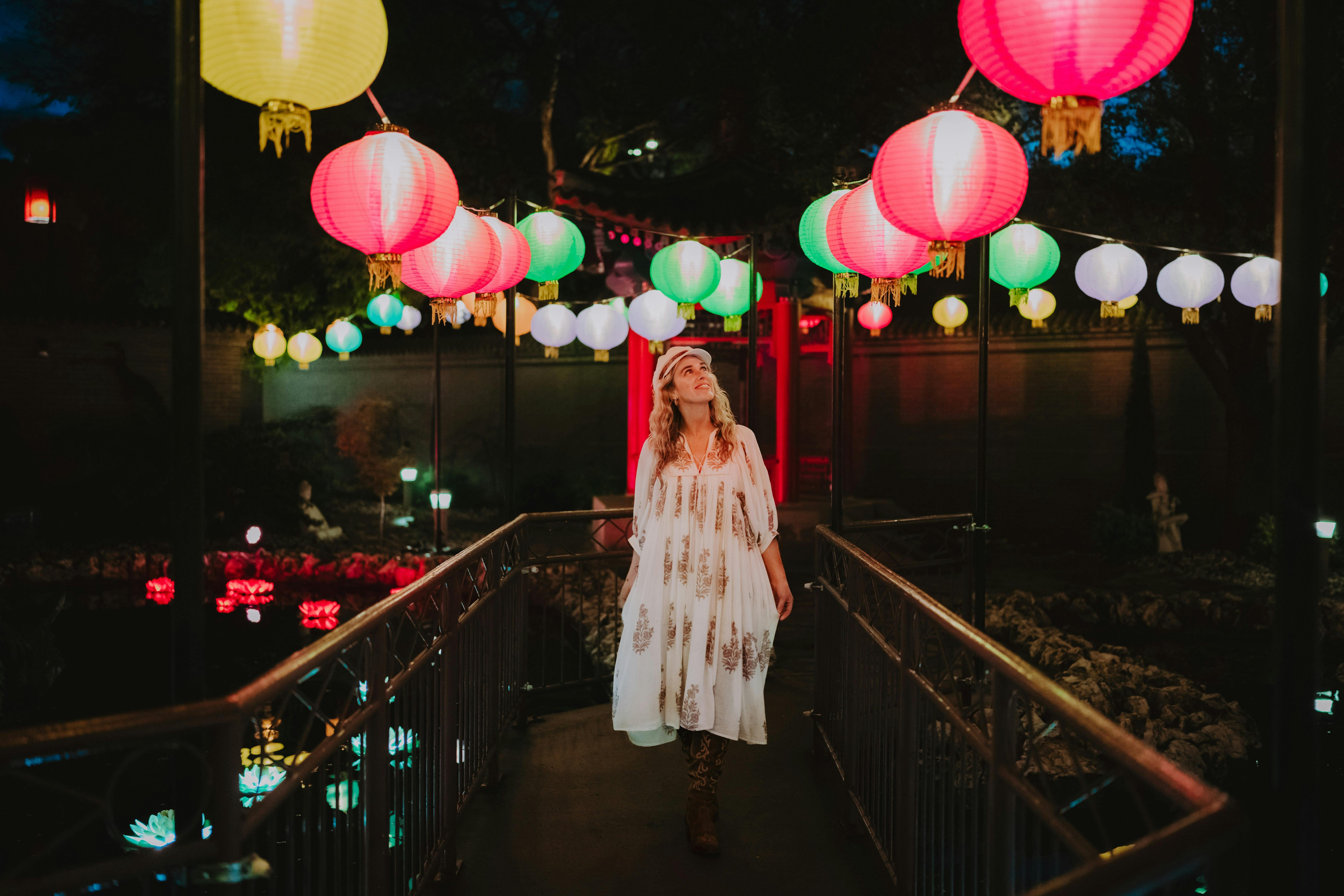 A lady walking down a path in the Yi Yuan Gardens at light. She's looking at rainbow lanterns
