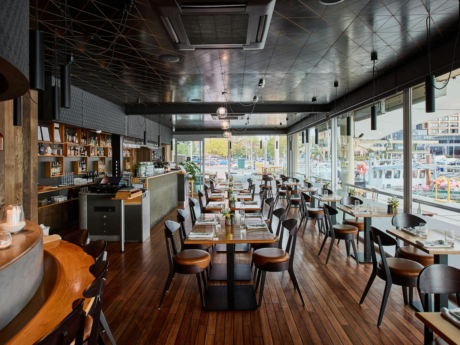 Restaurant interior with bar, tables and chairs, and floor to ceiling windows overlooking water