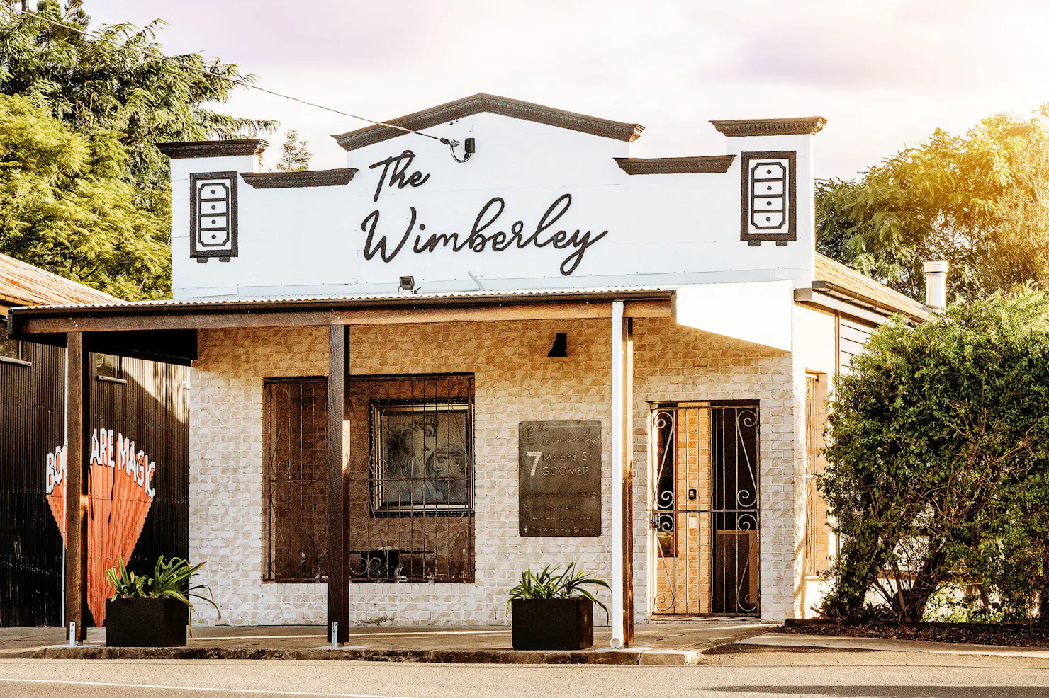 Street View and facade of brick building with decorative parapet and signage reading The Wimberley