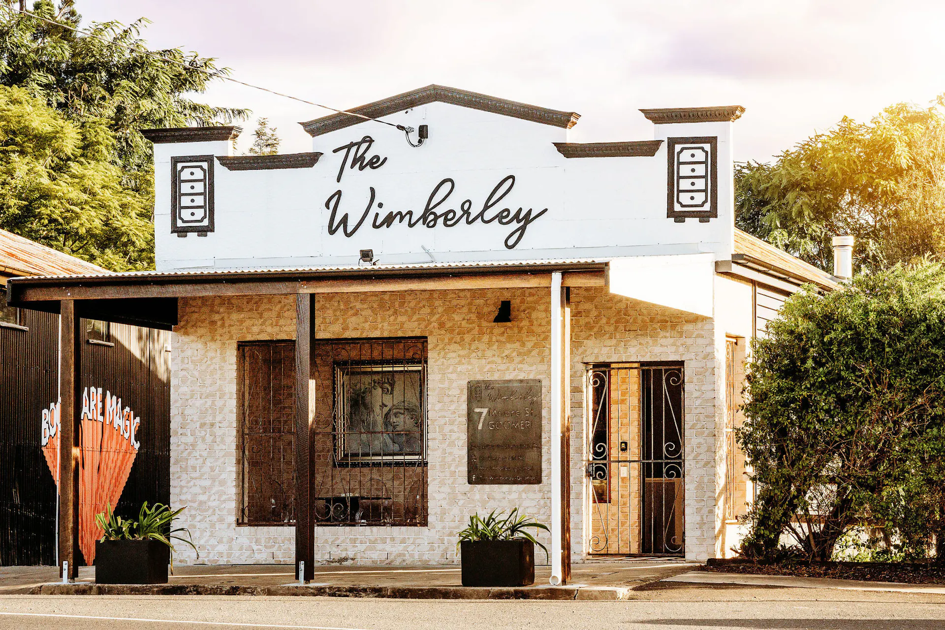 Street View and facade of brick building with decorative parapet and signage reading The Wimberley