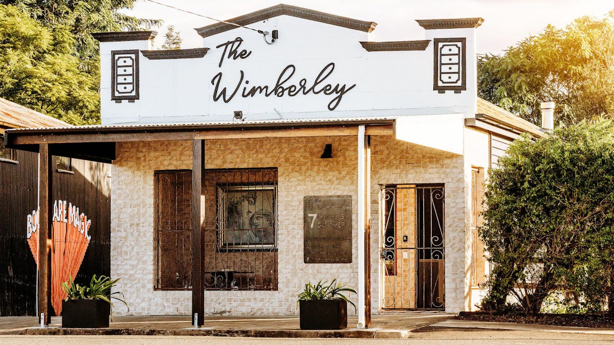 Street View and facade of brick building with decorative parapet and signage reading The Wimberley