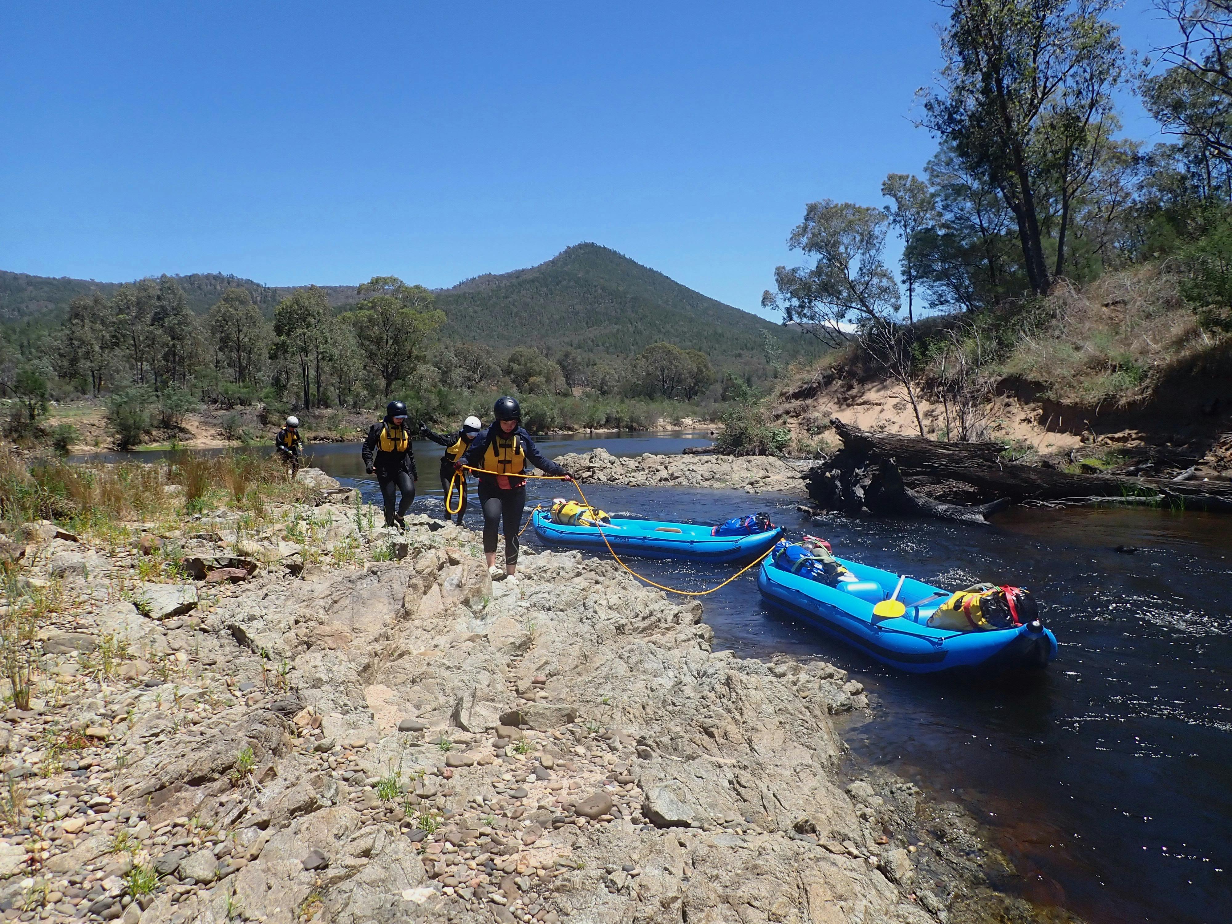 Two rafts on the Snowy River are being  held by ropes as people walk them   past a fallen tree.