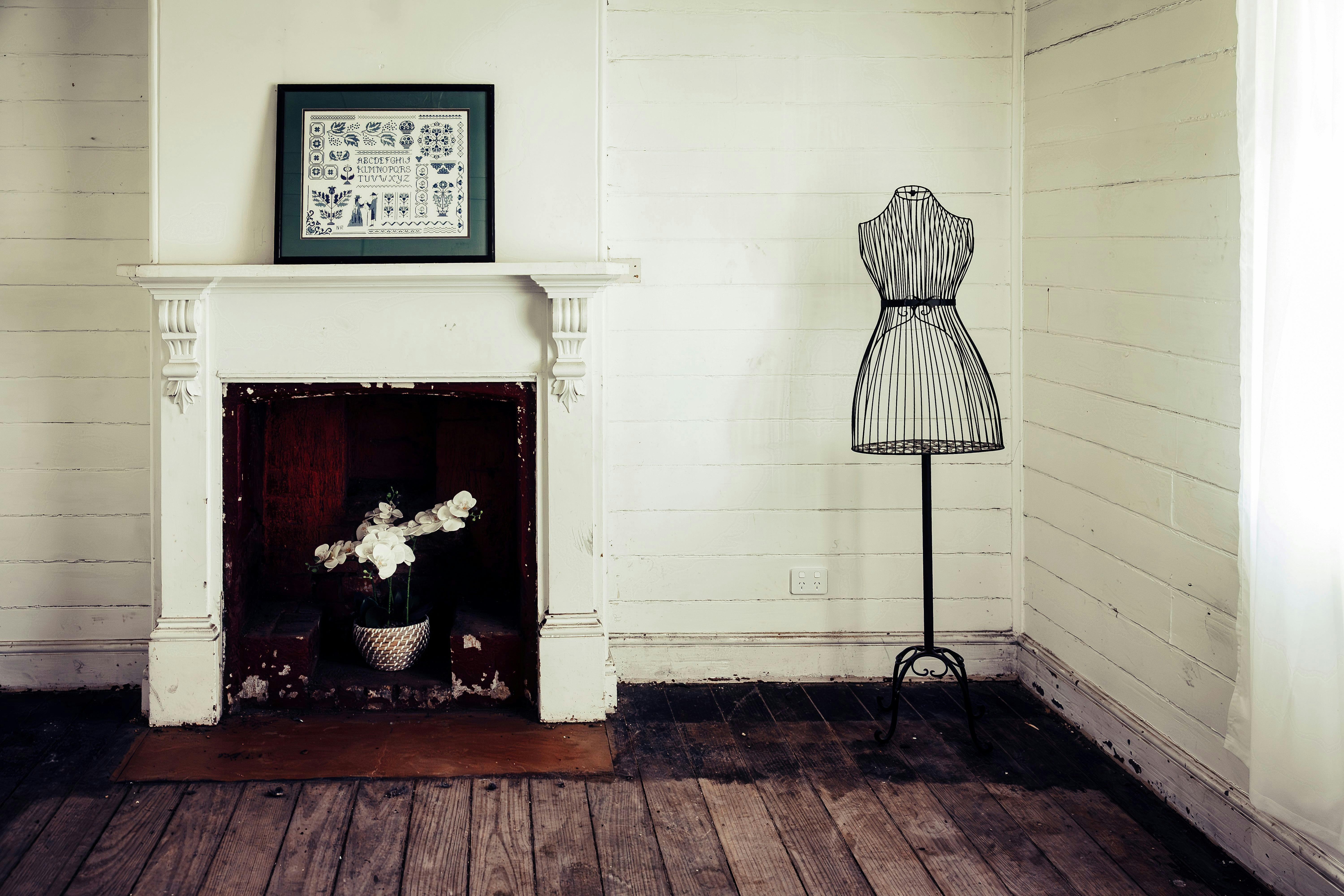 Interior of a room with timber floor, white walls and fireplace and a black dressmaker dummy