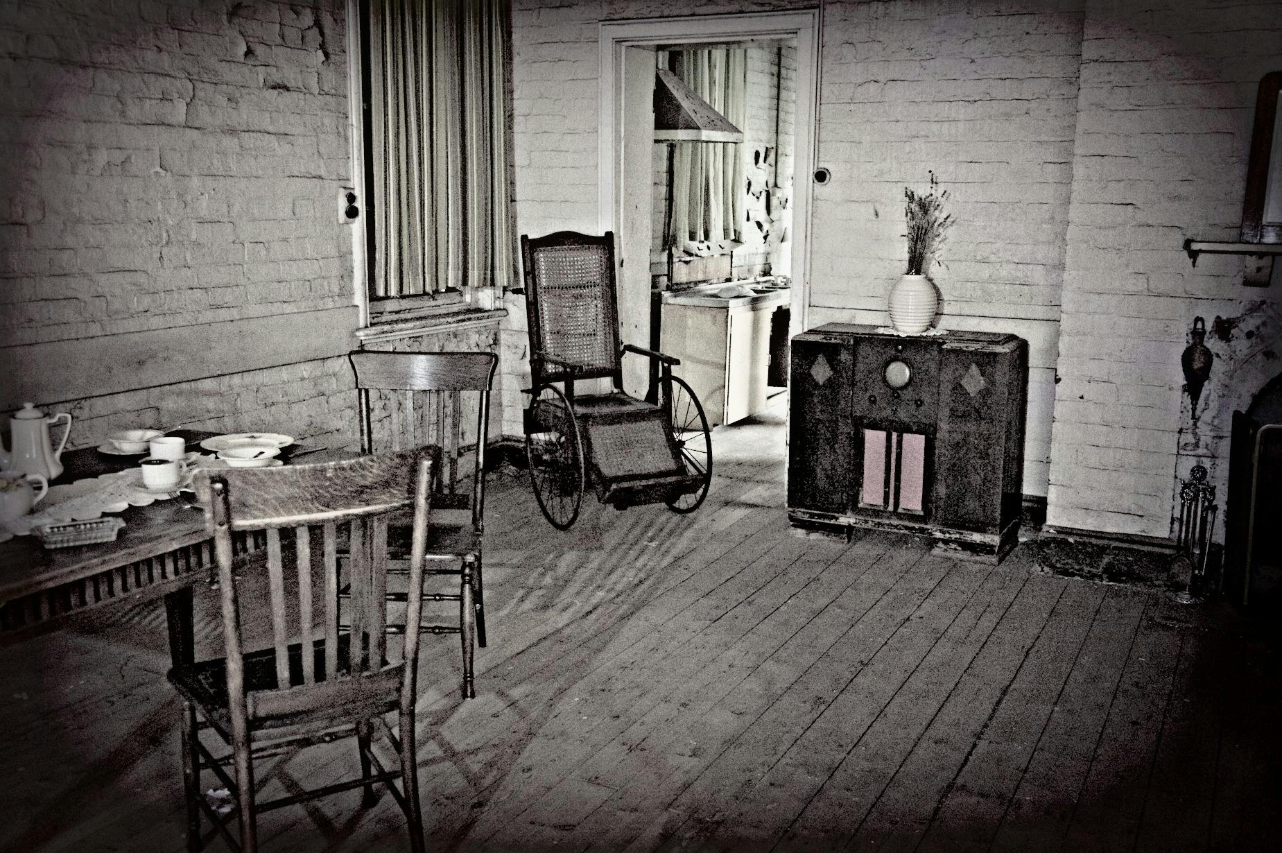 Inside asylum room. Chairs, table and wheelchair visible
