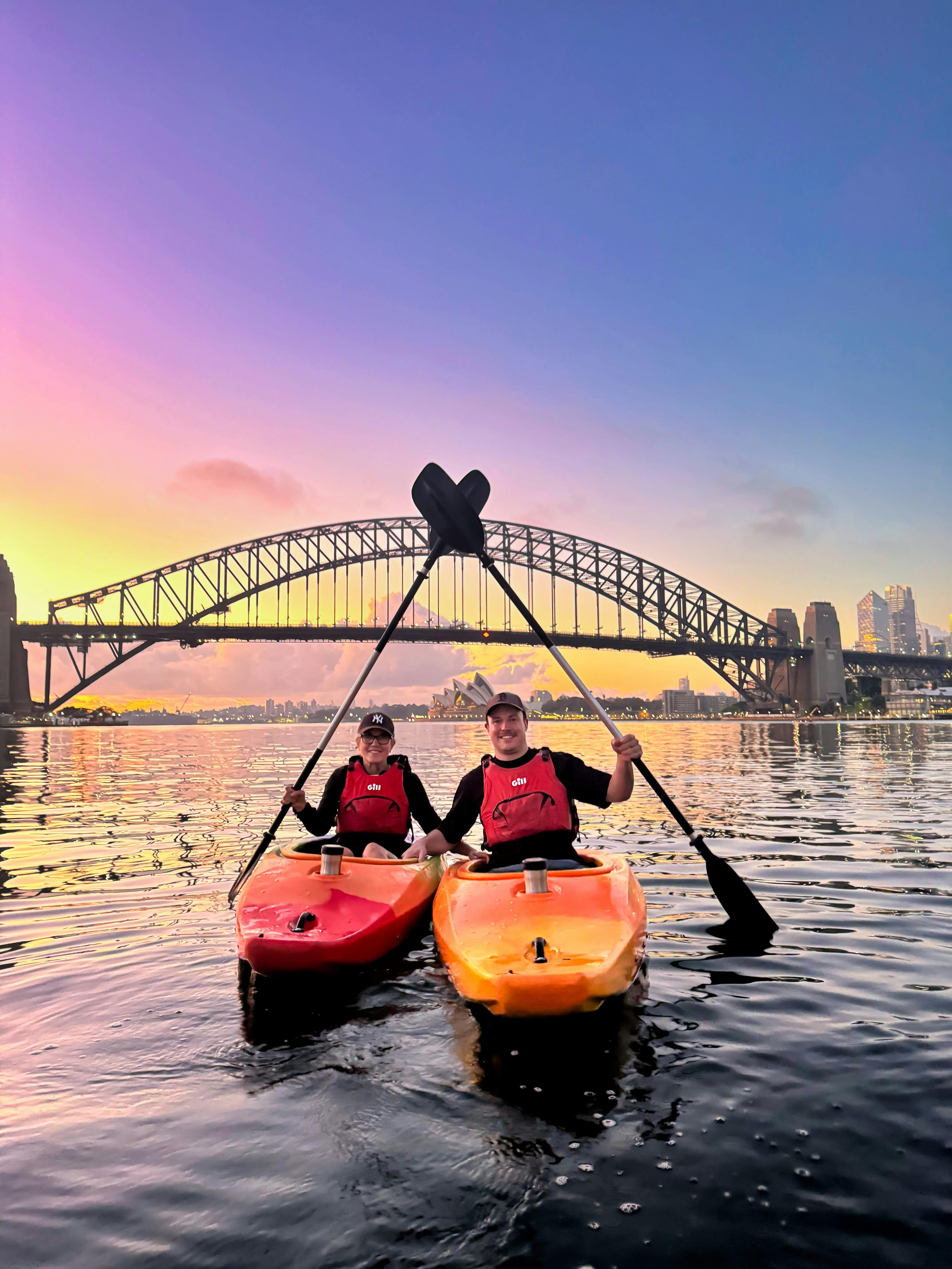 シドニー港で、シドニー・ハーバー・ブリッジとシドニー・オペラハウスを背景にカヤックを楽しむ2人