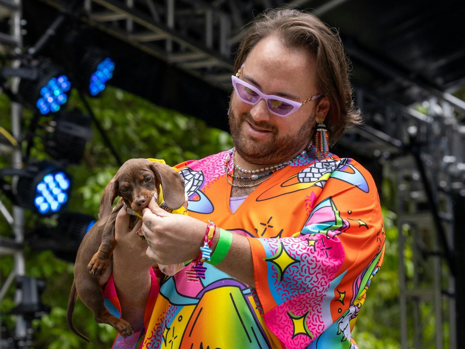 A colourfuly dressed person holds a small dachshund puppy, feeding the puppy a treat.