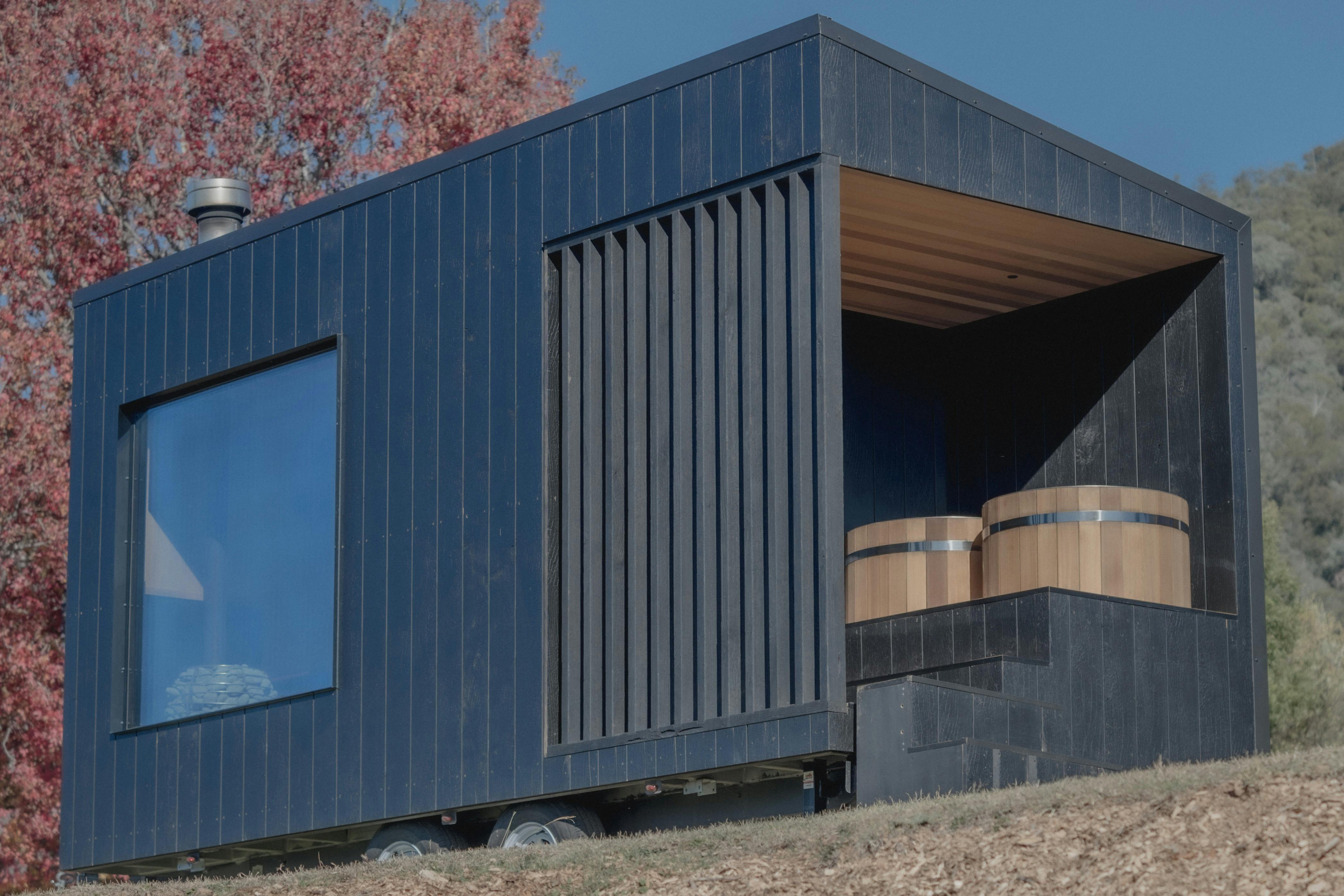 Large charred wood sauna in nature with cedar cold plunge tubs on deck and large sauna window