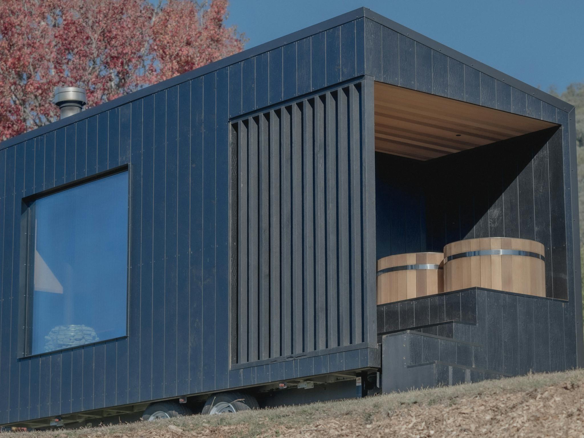 Large charred wood sauna in nature with cedar cold plunge tubs on deck and large sauna window