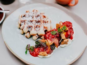 A white plate with Belgian waffles, roasted peach and strawberry, whipped yoghurt, honeycomb, shiso