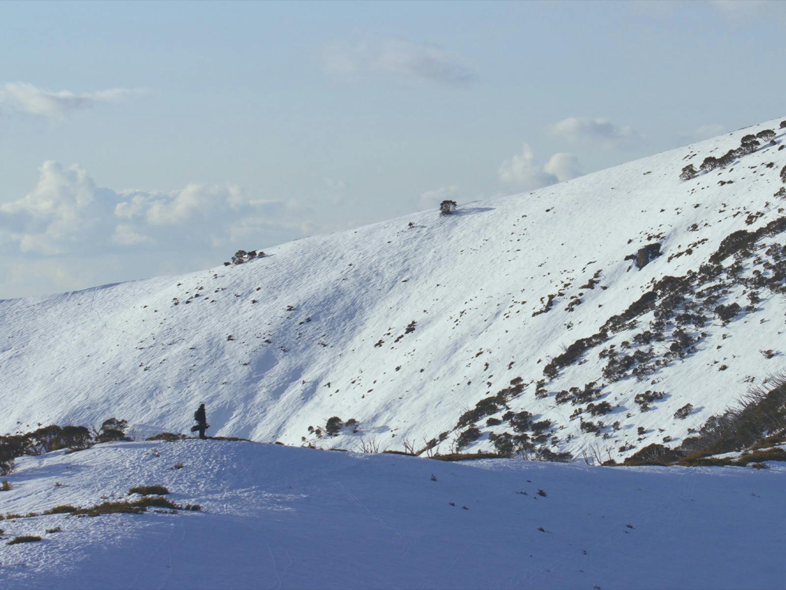 Lone person (Josef) walking across a vast snow-covered mountain landscape.
