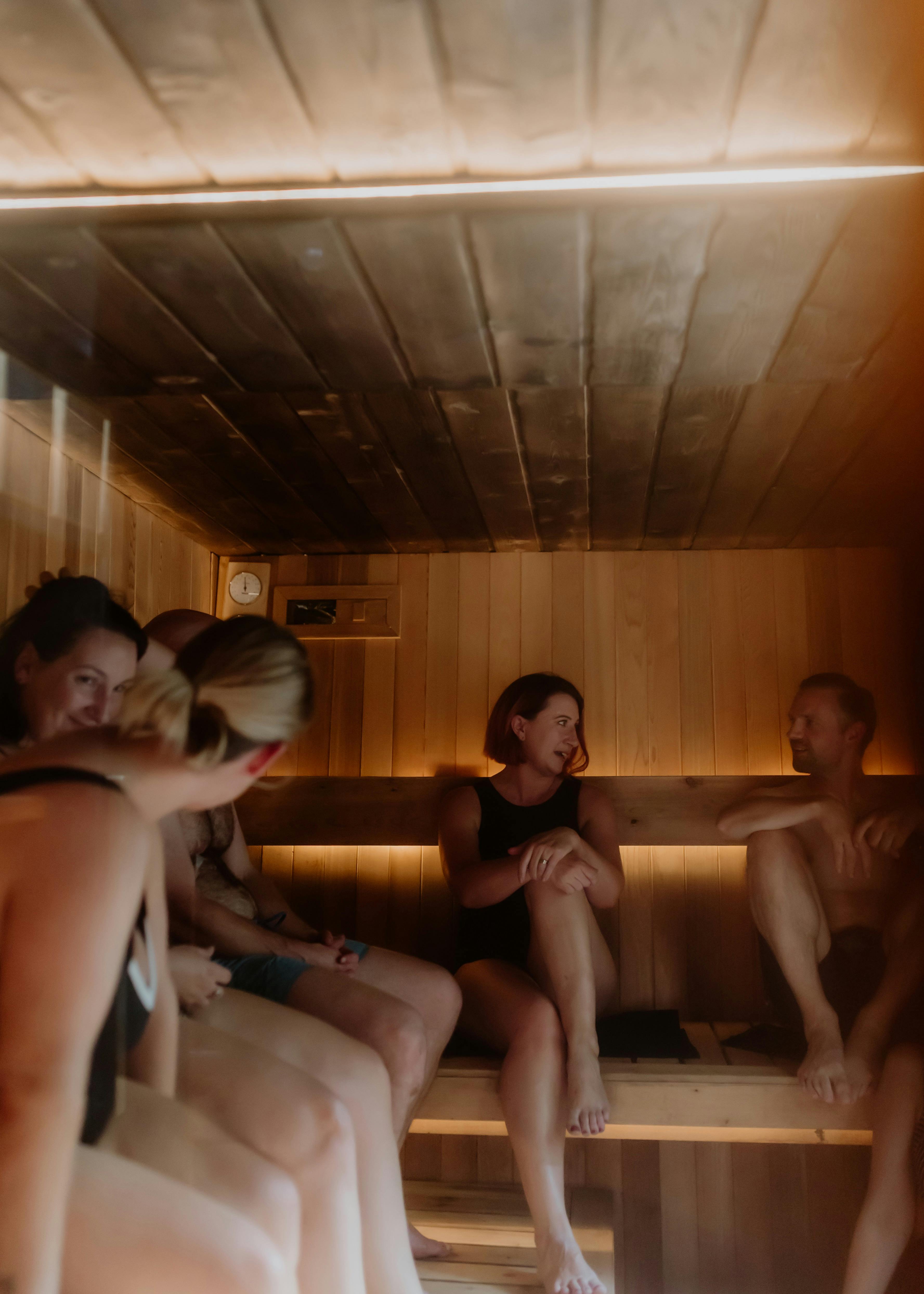 Guests seated together inside a warm timber-lined sauna illuminated by soft lighting.