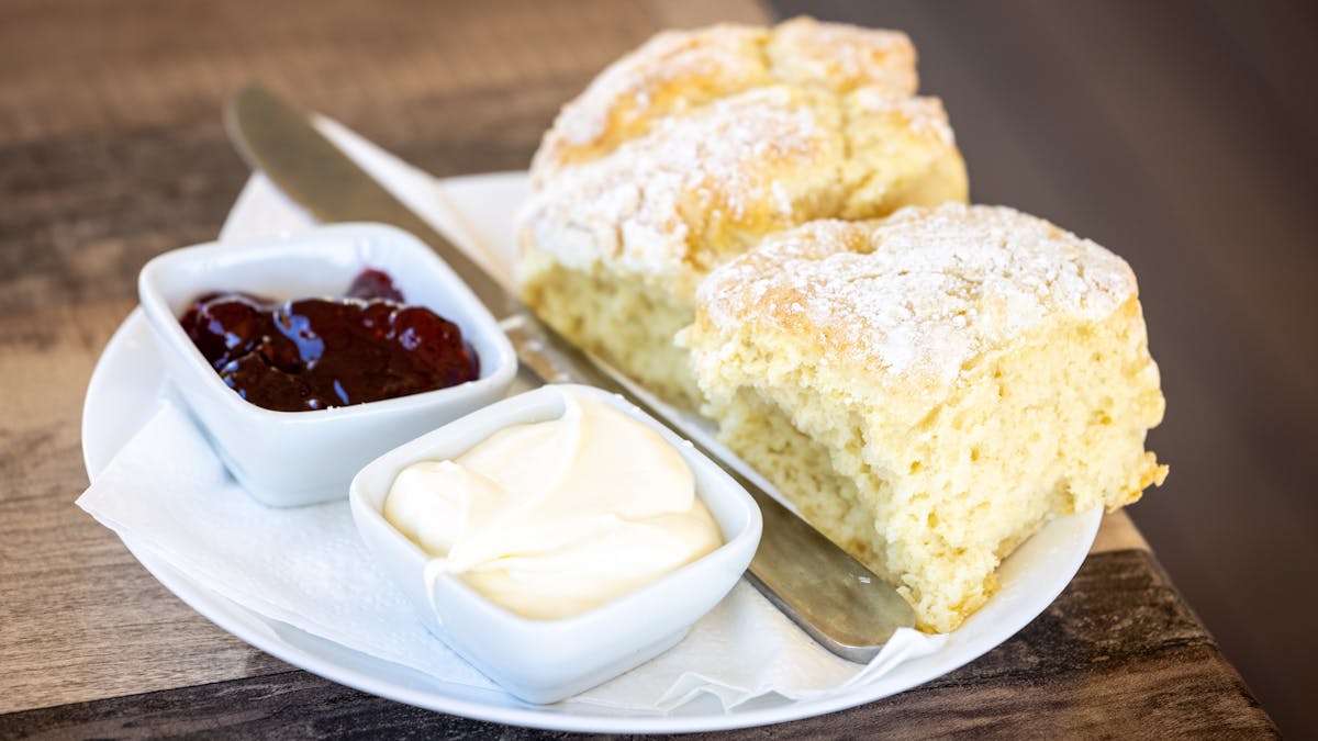 two scones on a plate with a knife,  a pot of jam and a pot of cream