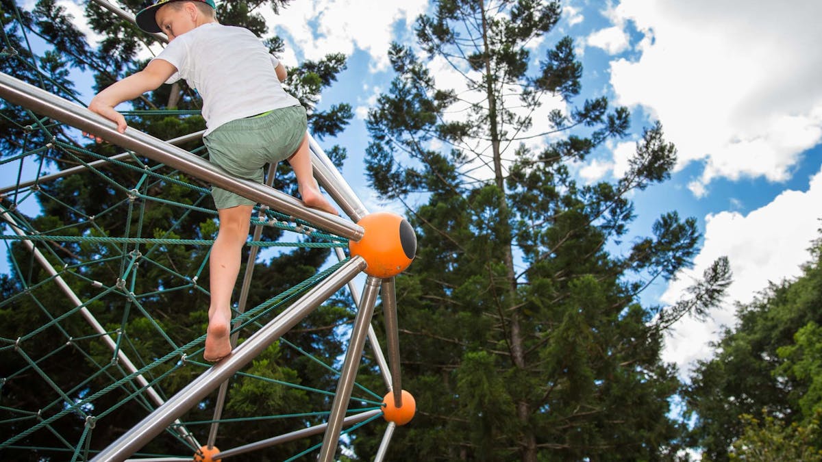 Young teenage boy nearing the top of a climbing frame made with ropes