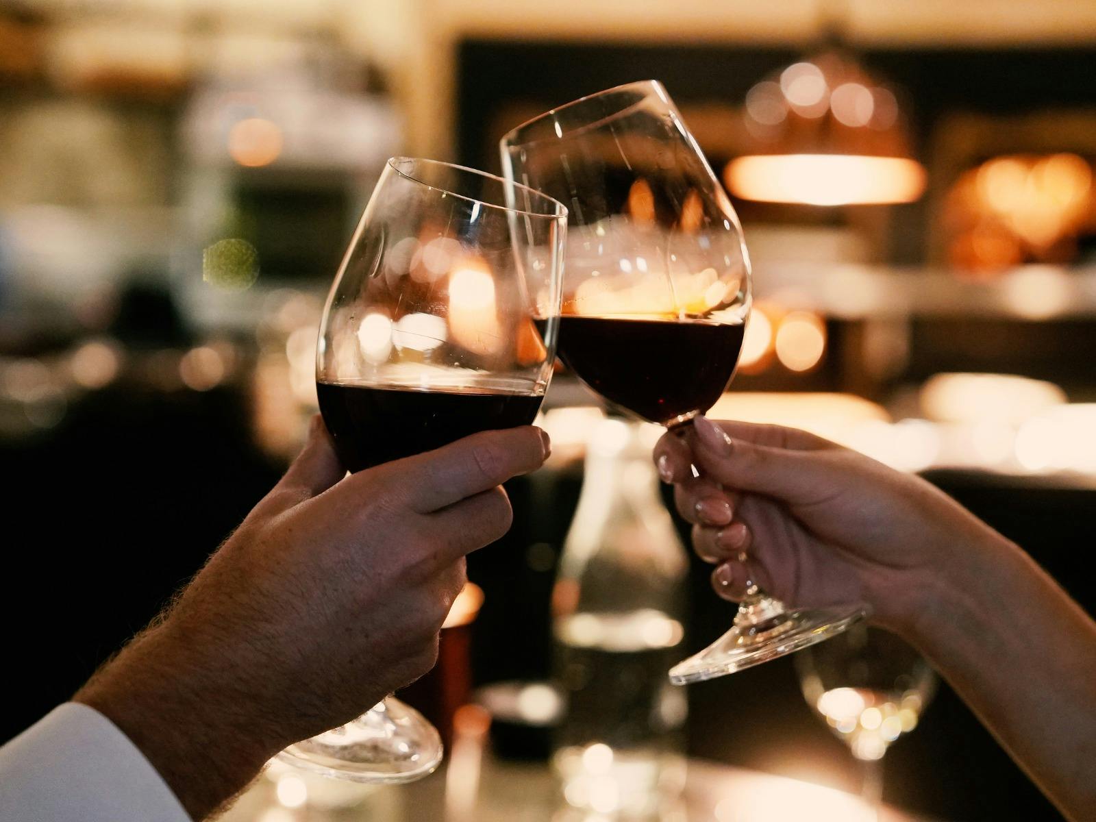 Couple clinking two glasses of red wine in The Fireplace with the fire in the background