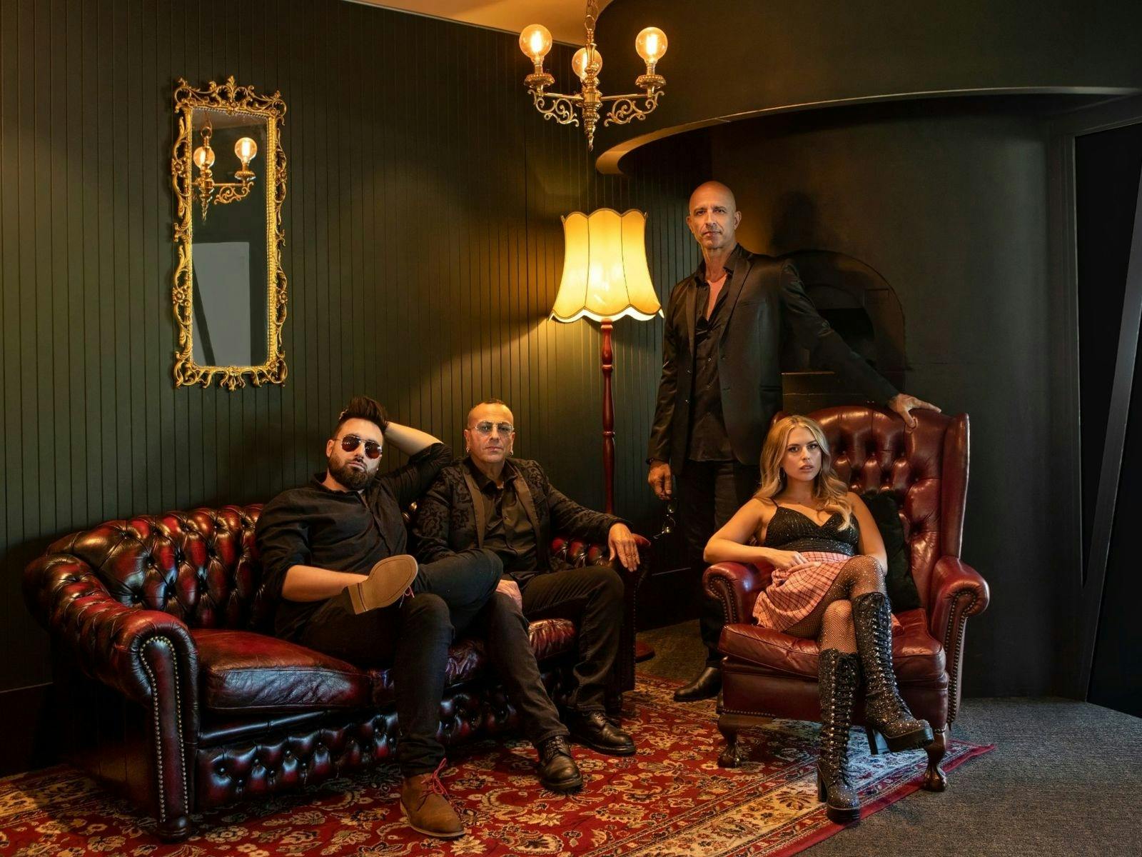 Dark image of 4 artists 2 seating on a  couch  and female on a seat male standing behind