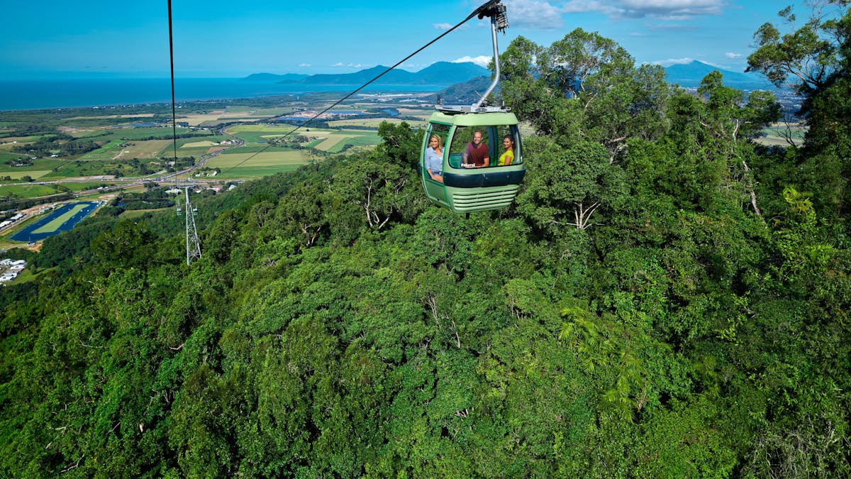 Skyrail gondola over rainforest with 3 people and blue sky