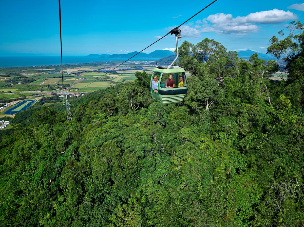 Skyrail gondola over rainforest with 3 people and blue sky