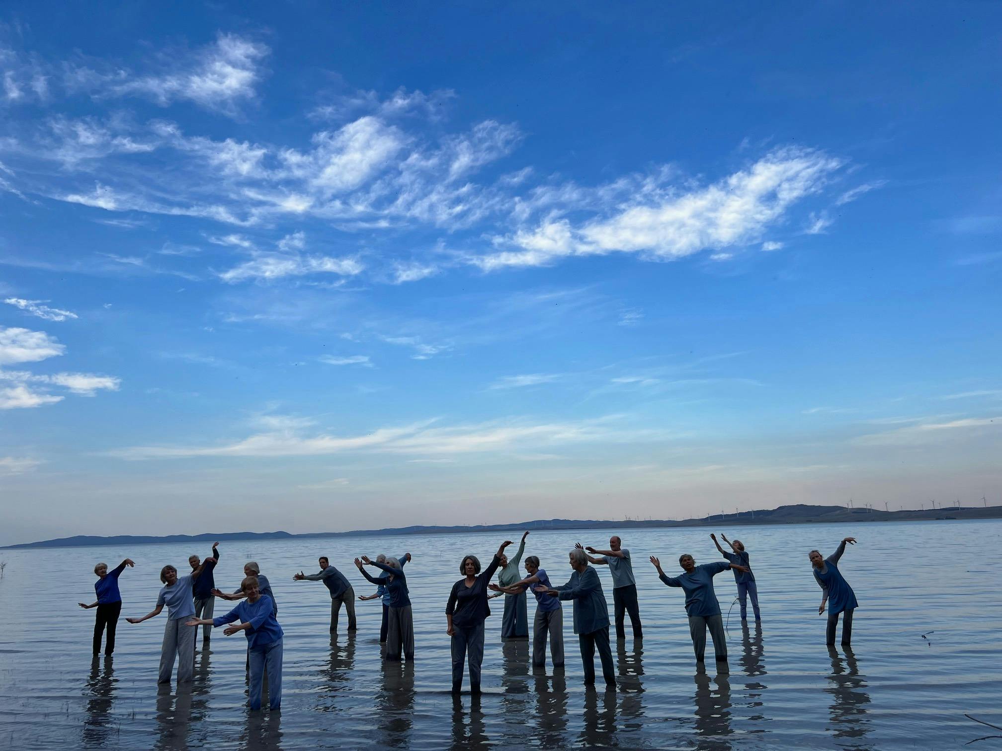 14 people standing knee deep in an expanse of water with a bright blue sky and fluffy white clouds