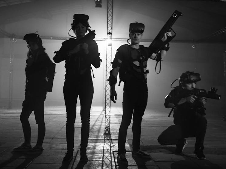 Four people holding guns wearing virtual reality equipment