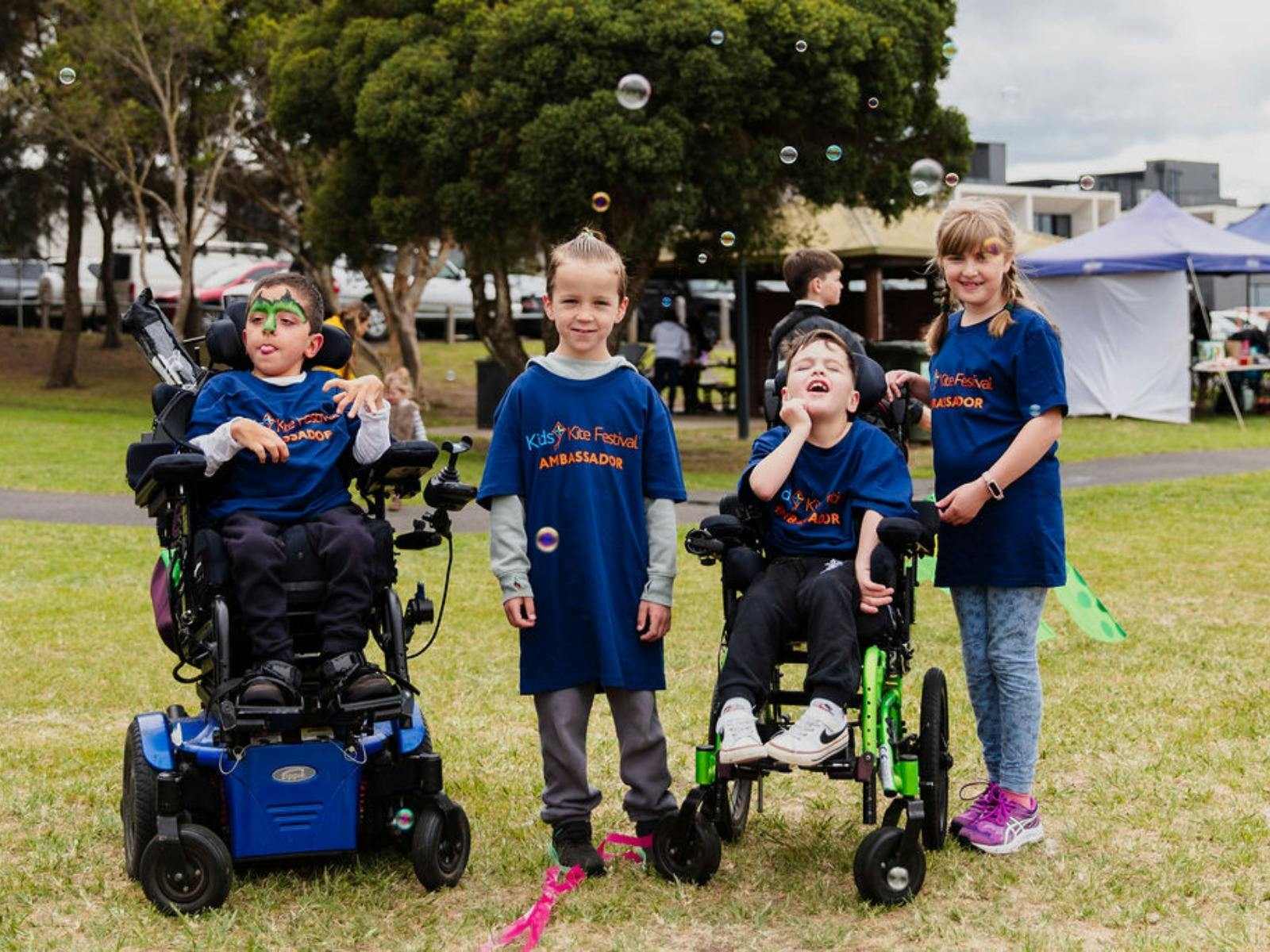 A group of 4 children, 2 wheelchair users, all wearing Ambassadors tees, are smiling