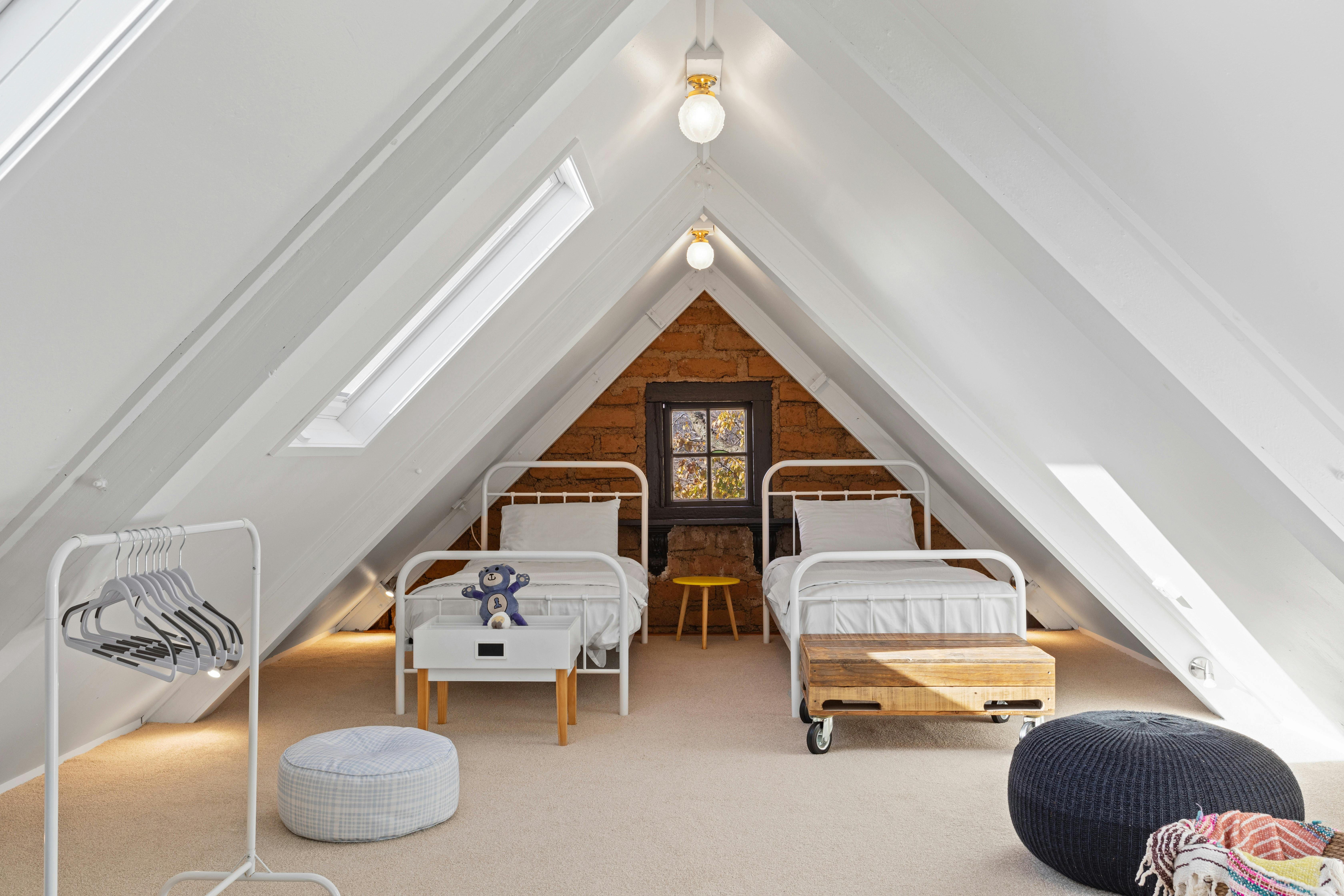 Loft bedroom with two single beds and floor cushions, lit by skylights