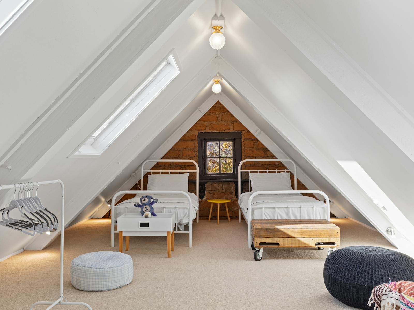 Loft bedroom with two single beds and floor cushions, lit by skylights