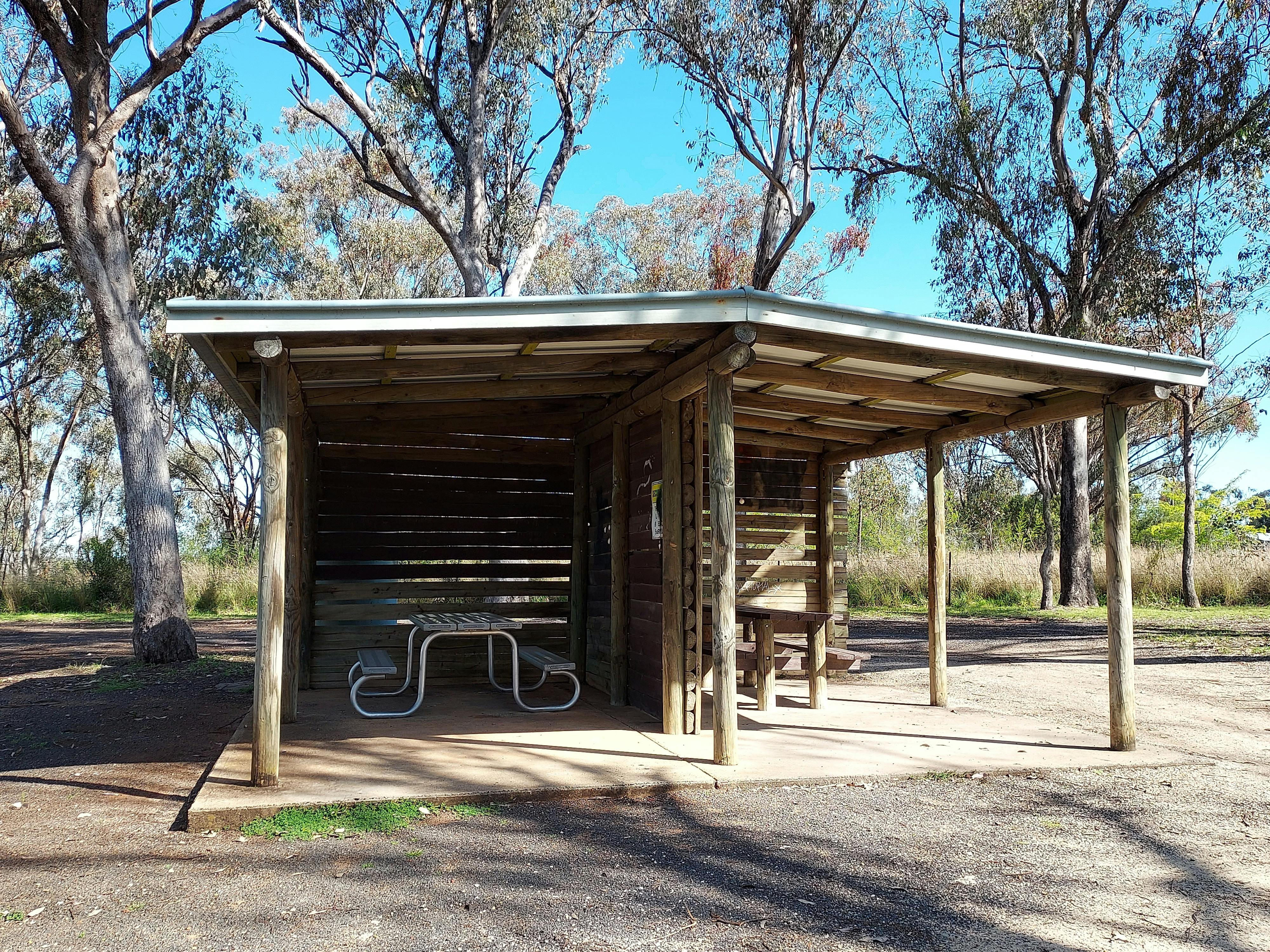 Shelter with two picnic tables divided by a wall with gum trees behind the shelter.