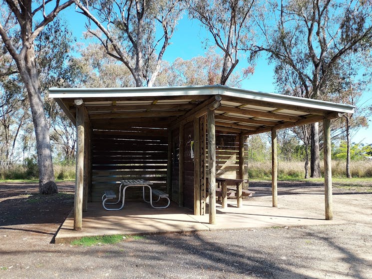Shelter with two picnic tables divided by a wall with gum trees behind the shelter.