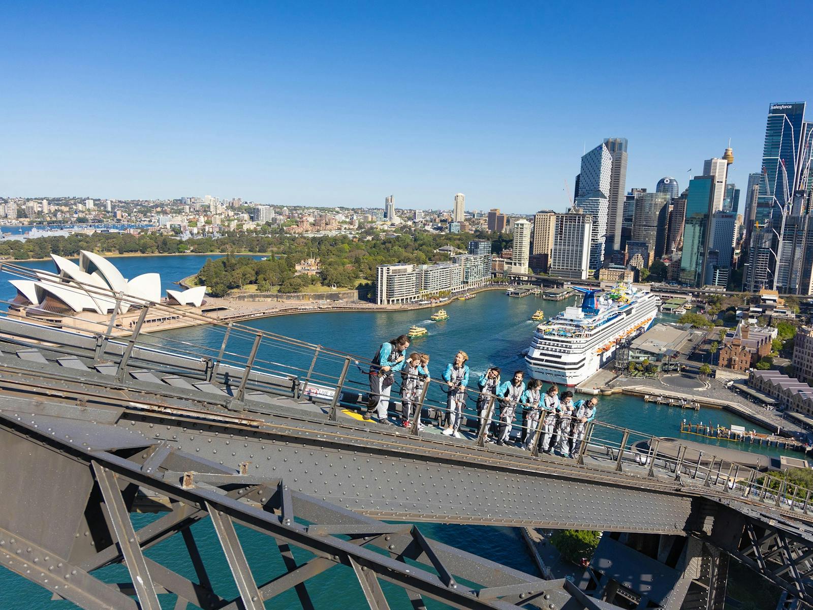 A group of Climbers walking up the upper arch of the Sydney Harbour Bridge with the Harbour behind