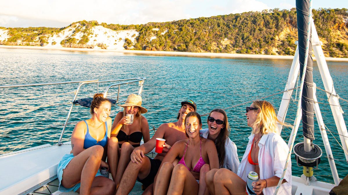 Group of charterers relaxing on the front deck of the catamaran along K'gari - Fraser Island.