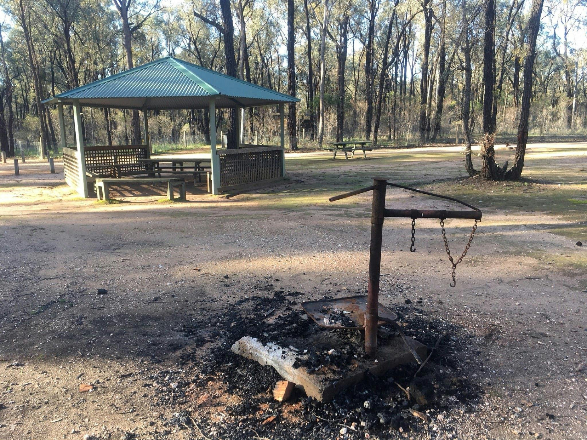 Rotunda, fire pit, table, trees, grass, sunny day.