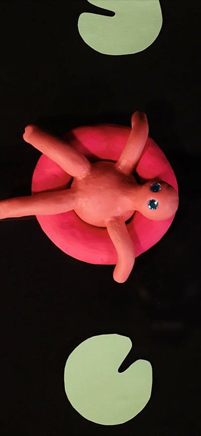 A video still image of a pink clay character sitting in a pool float surrounded by green lily-ads