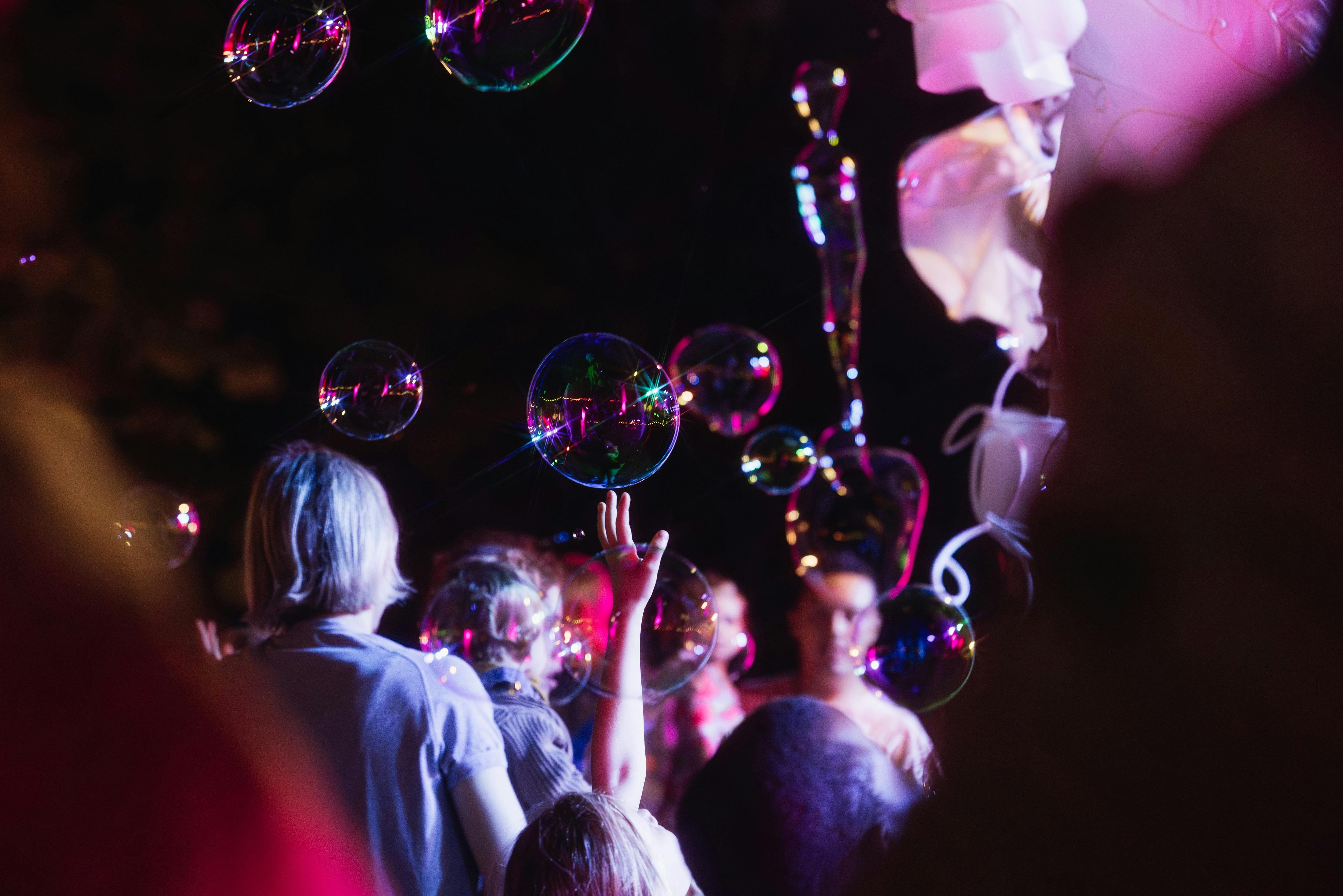 A childs hand reaching up to touch a bubble at night