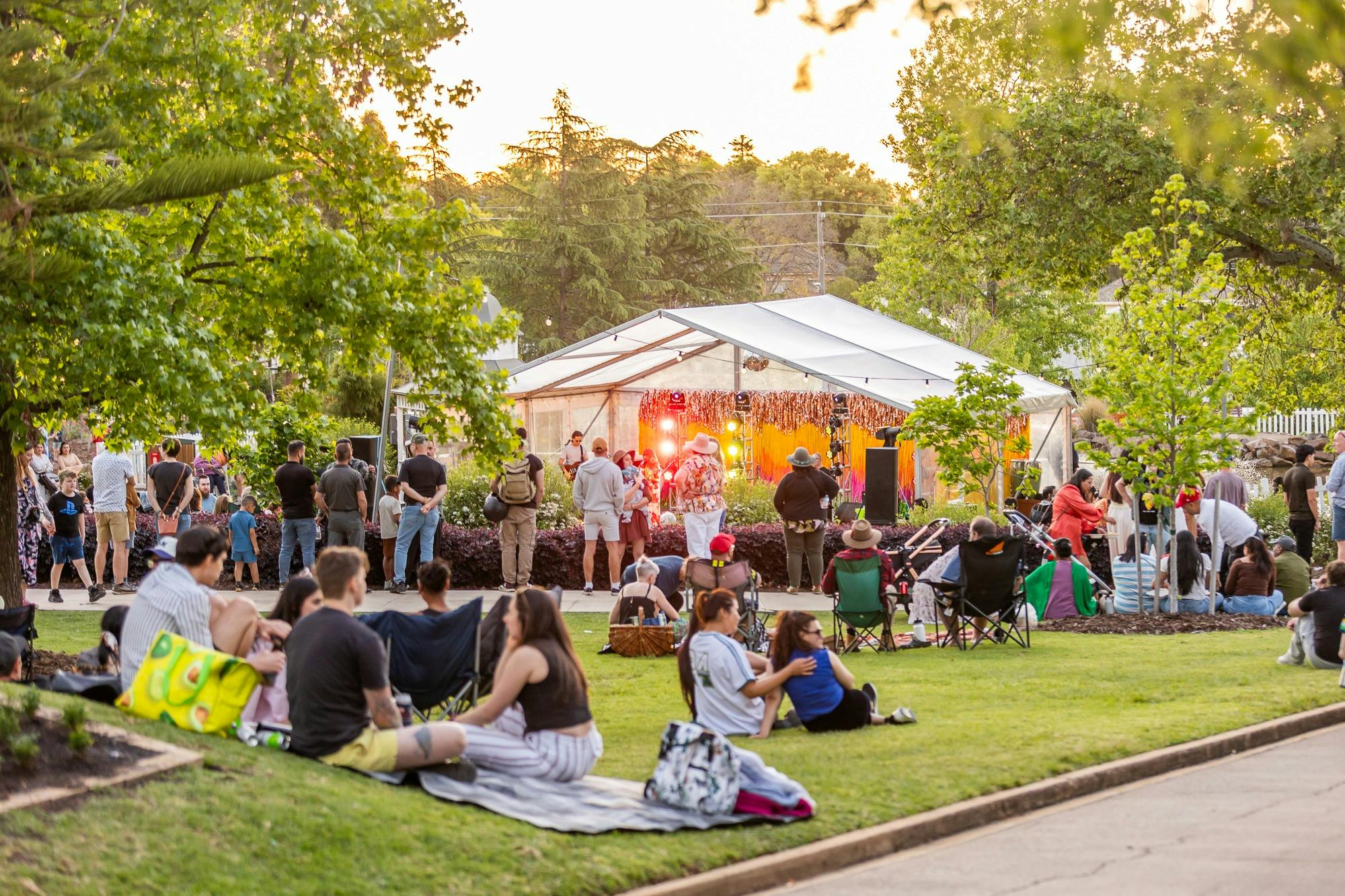 A spring day with people seated on teh green grass looking onto a festival stage with a band perform