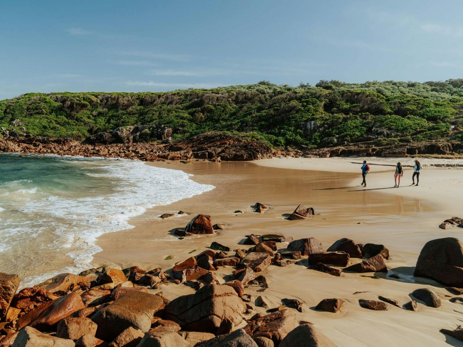 People walking on a Little Kingsley beach with forest in the background
