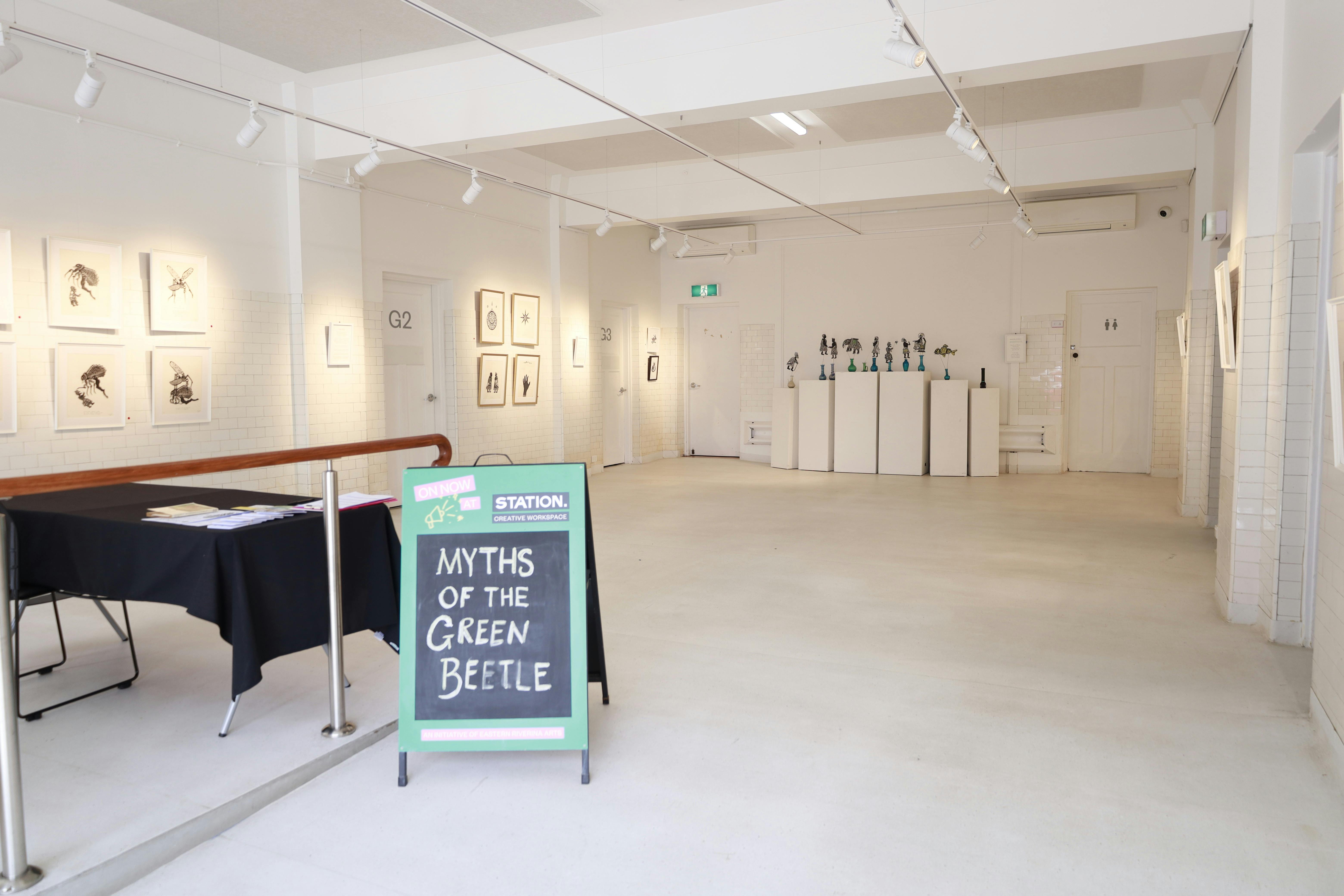 Gallery space consisting of white tile walls and hanging system, and white plinths with artworks.