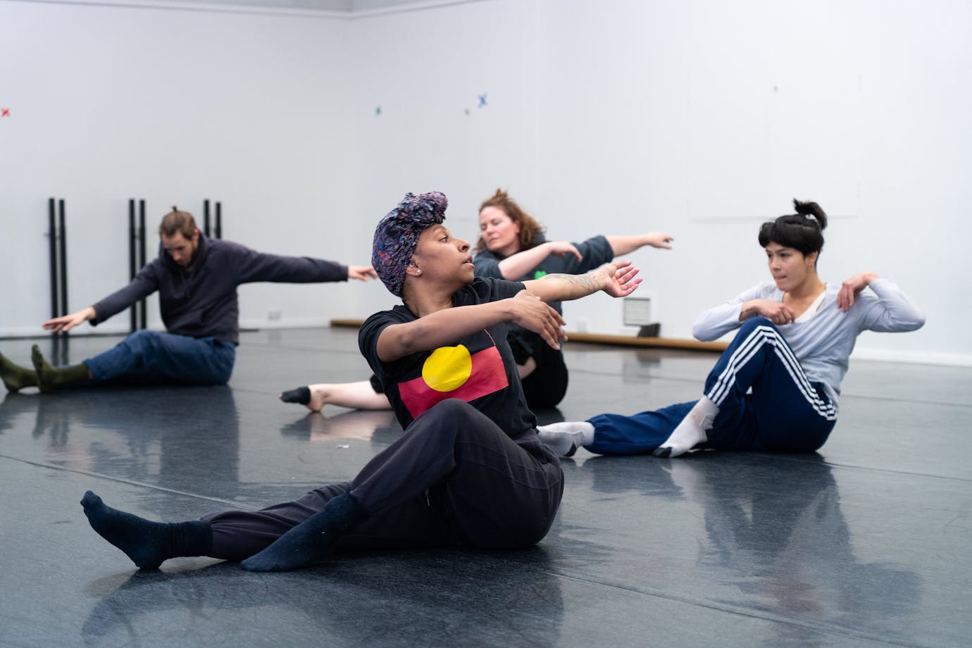 4 dancers are in the middle of twisting towards the camera. They are seated on the floor