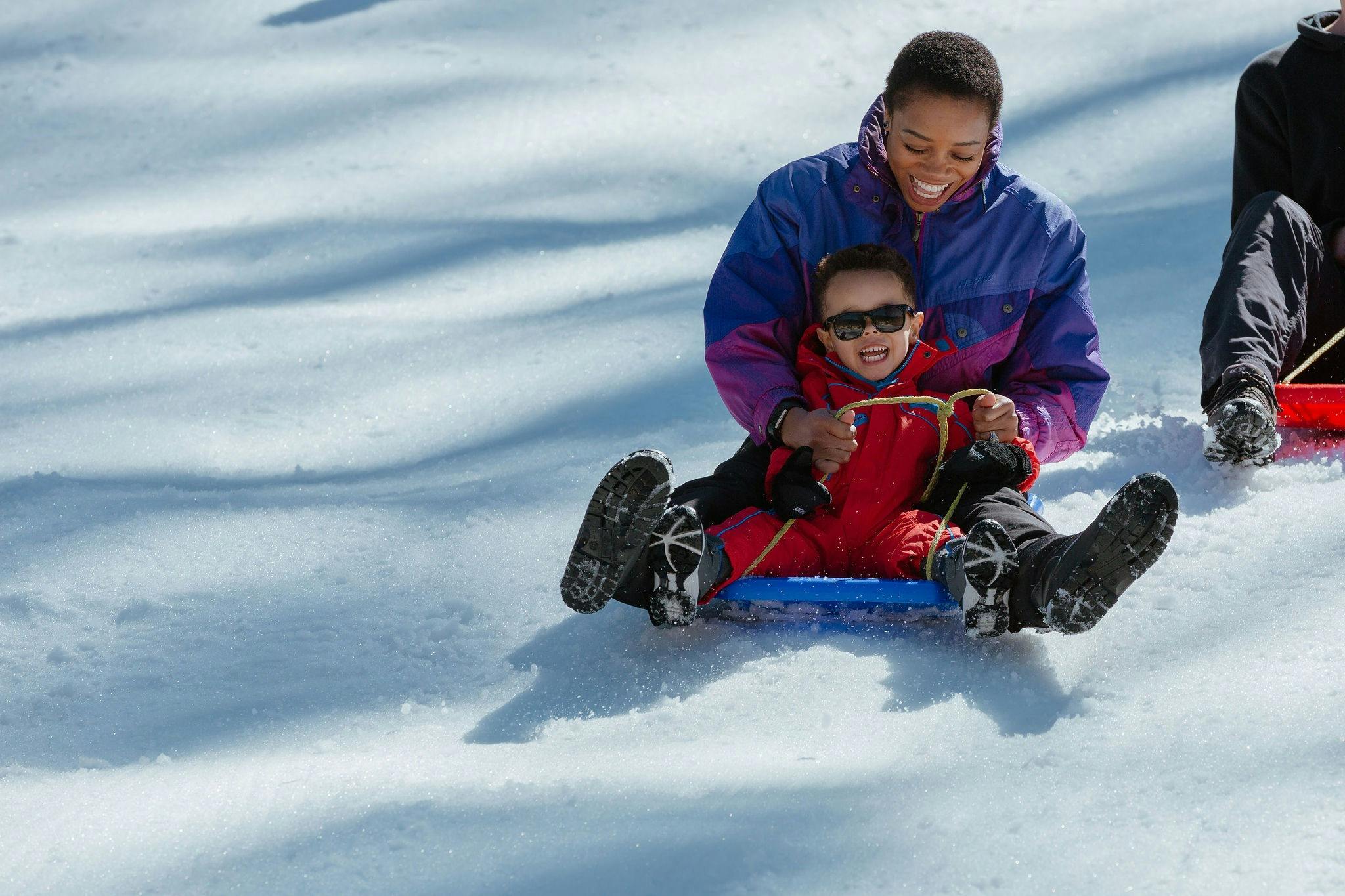 A mother and son riding a toboggan down a slope covered in snow, with big smiles on their faces.