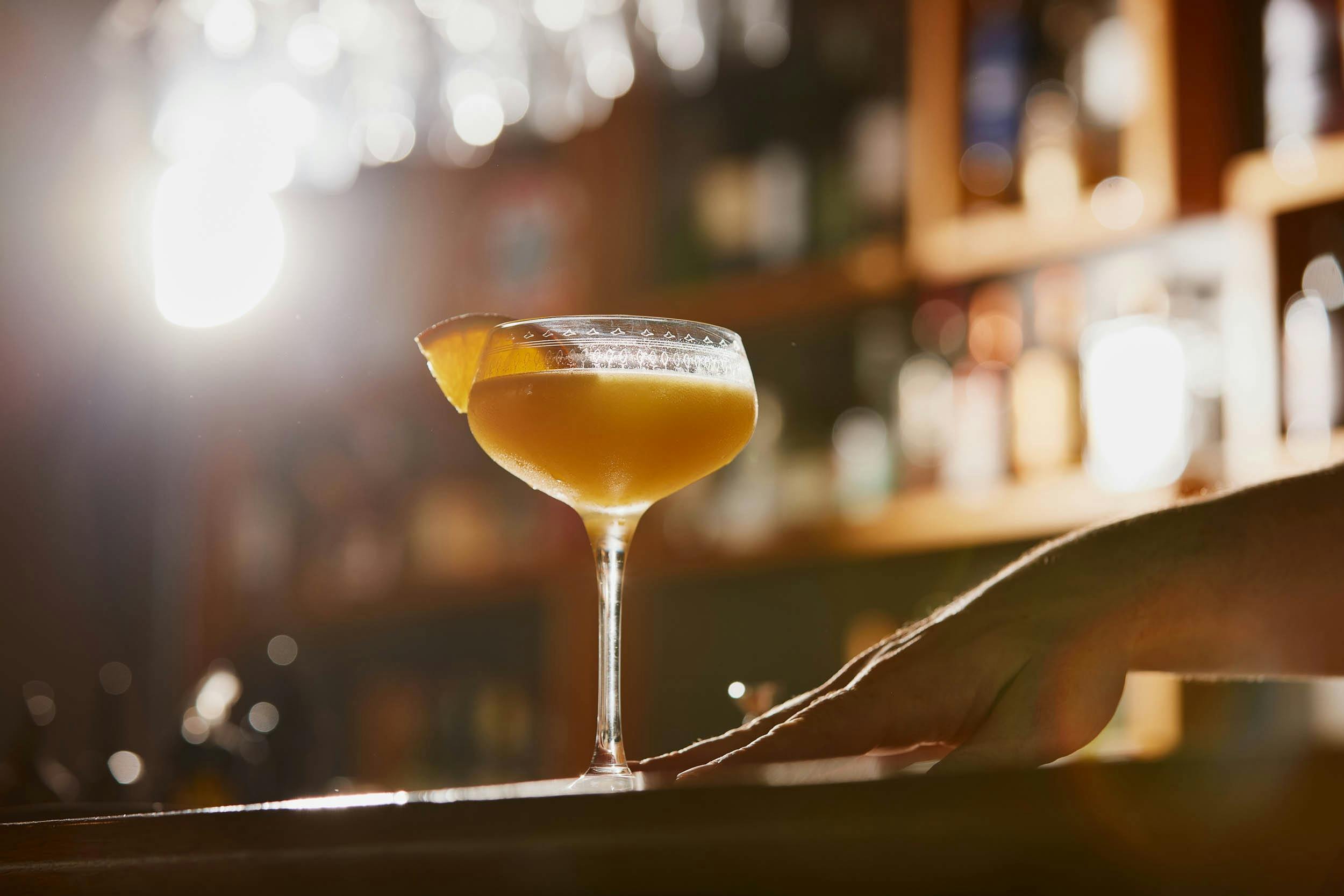 A bartender sliding a Sidecar cocktail across a counter, garnished with an orange slice