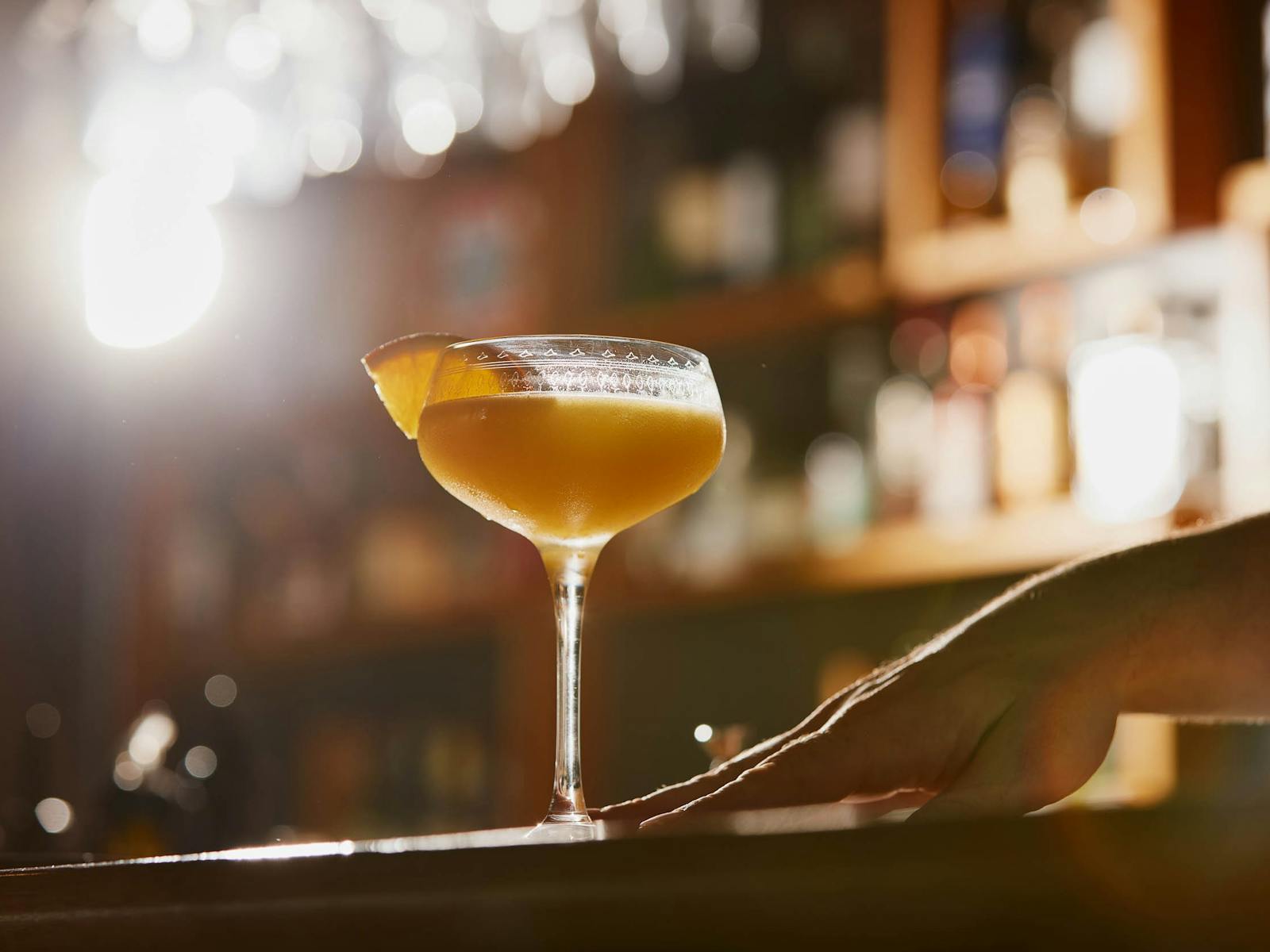 A bartender sliding a Sidecar cocktail across a counter, garnished with an orange slice
