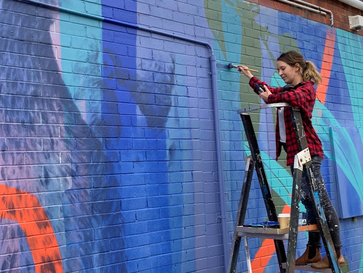 Claire painting a mural as part of the REVIVE mural project