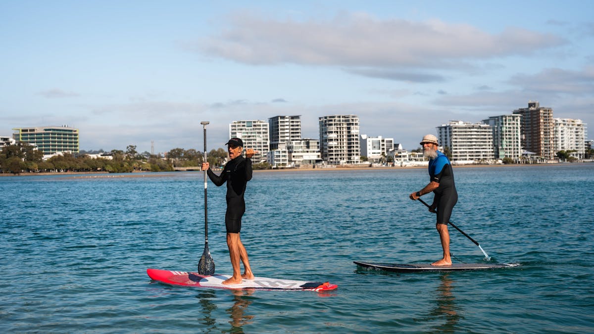 Image of 2 men riding stand up paddles board in Cotton Tree river side