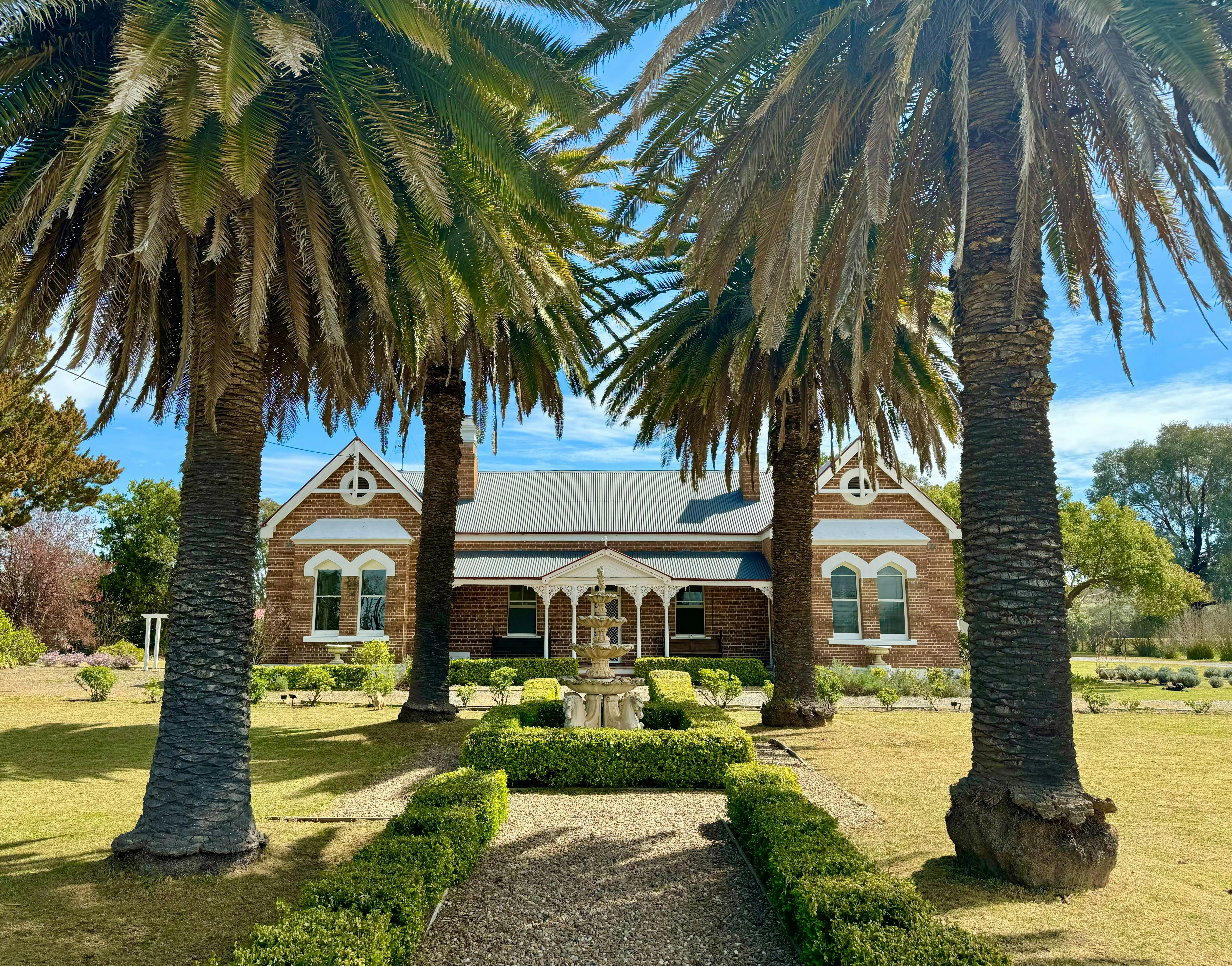 Ceremonial entrance to large house, with fountain and four large palm trees.