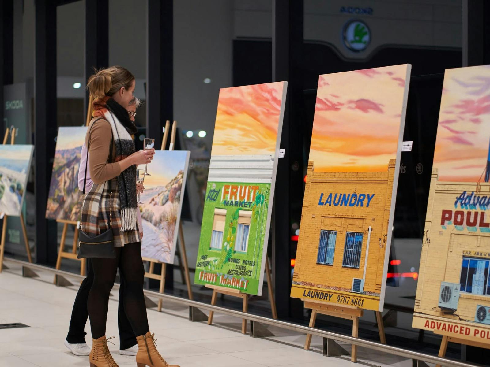 Woman viewing Donovan Christie shopfront paintings displayed on easels.