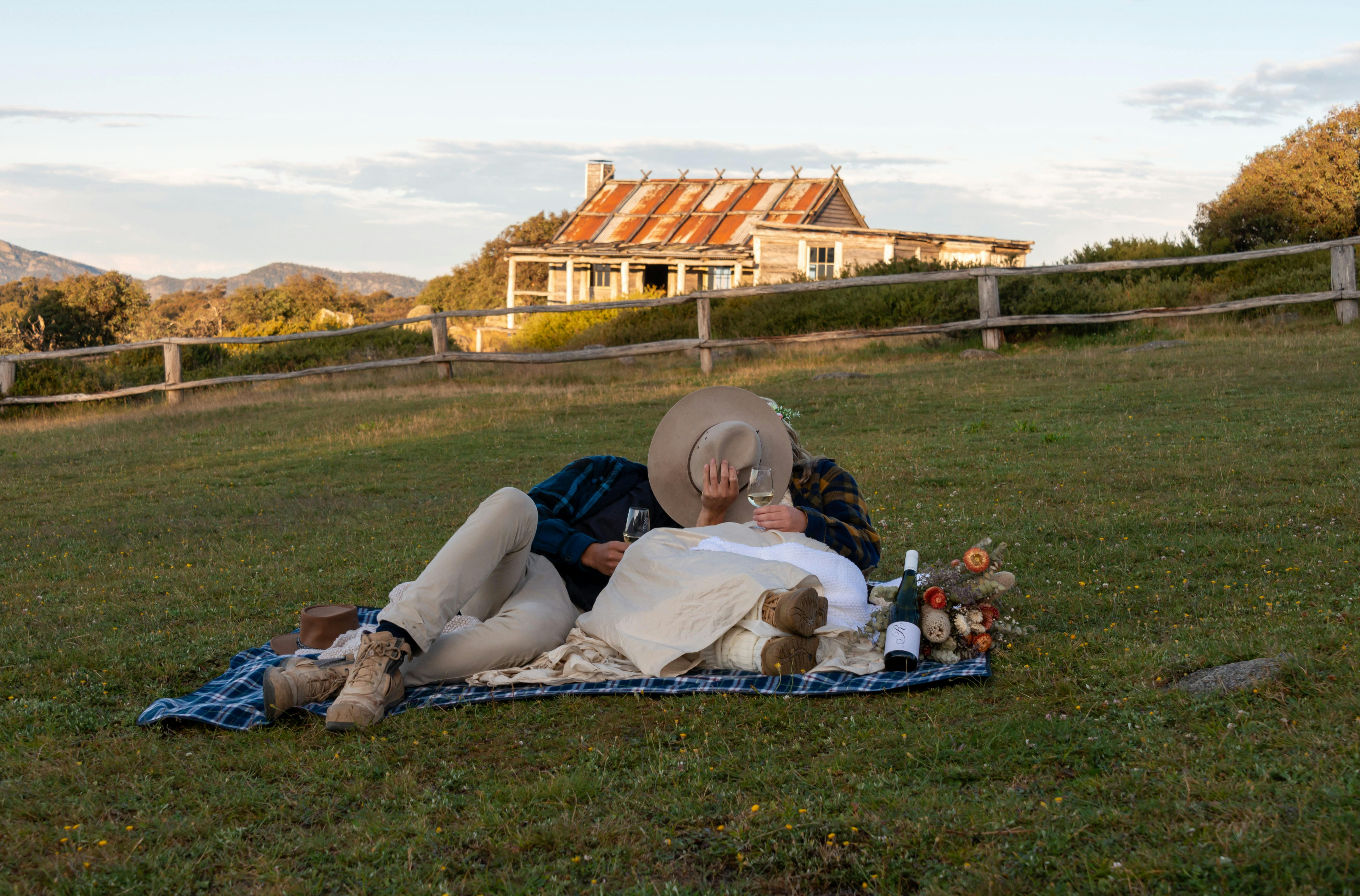 Just married couple relaxing on a picnic blanket in front of Craig's Hut with a glass of wine.